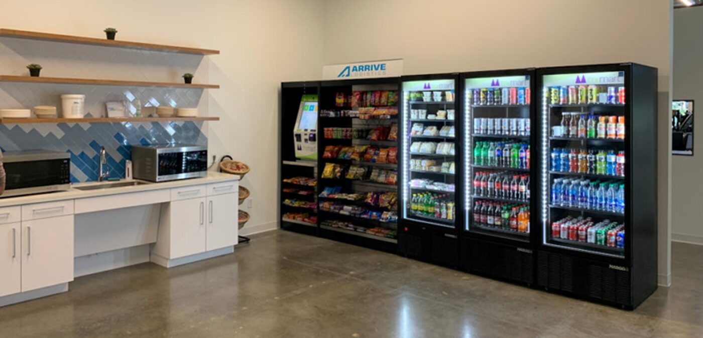 The Arrive Logistics break room: a branded micro-market kiosk, snack shelving and three lit coolers beside a counter with microwaves.